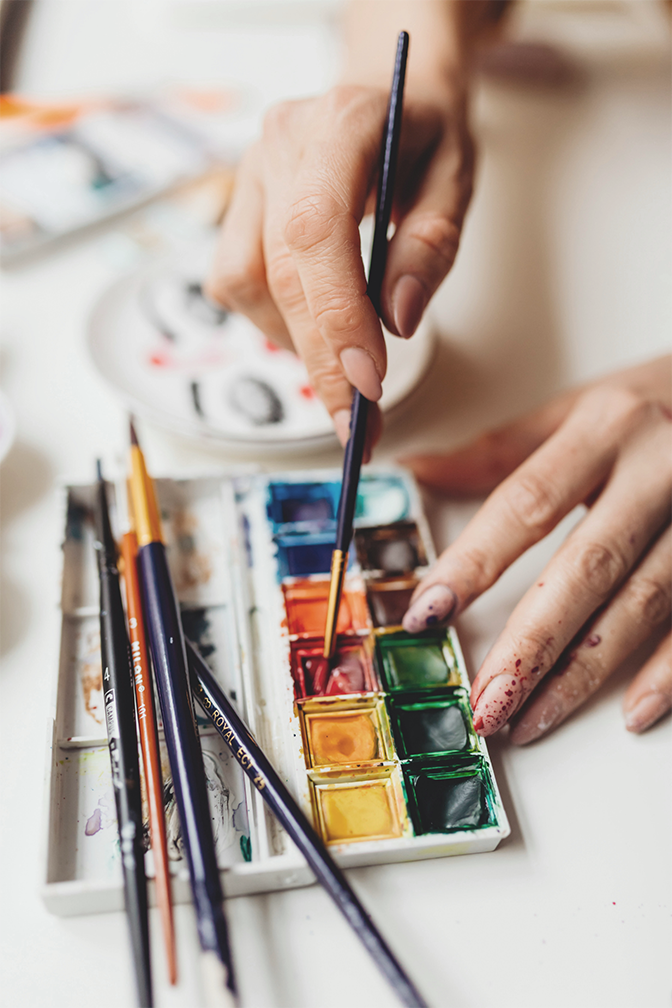 Des mains mélangent de la peinture à l’aquarelle au pinceau dans une palette.