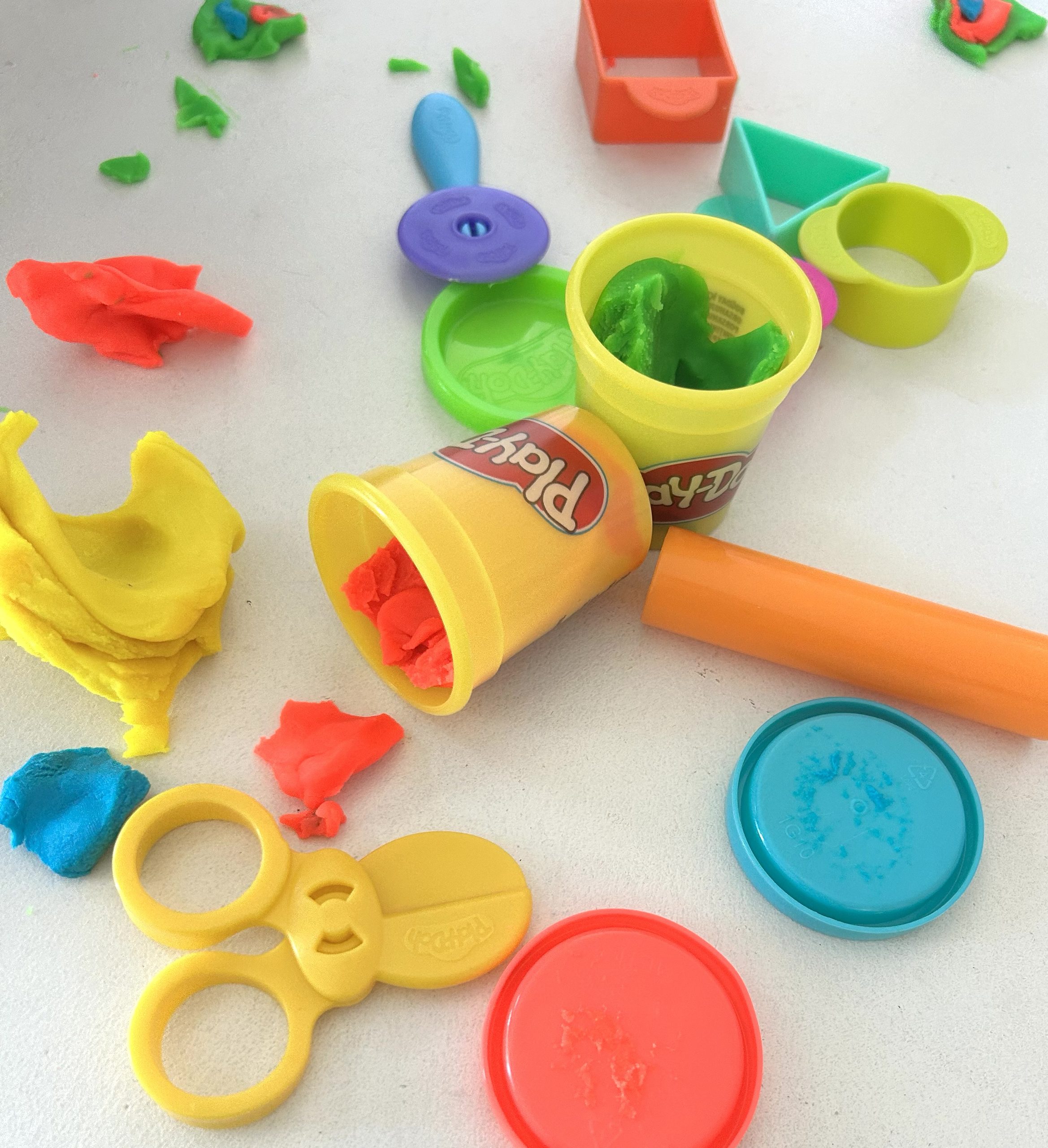 Pots de pâte à modeler colorée, rouleau, ciseaux et petits outils disposés sur une table.