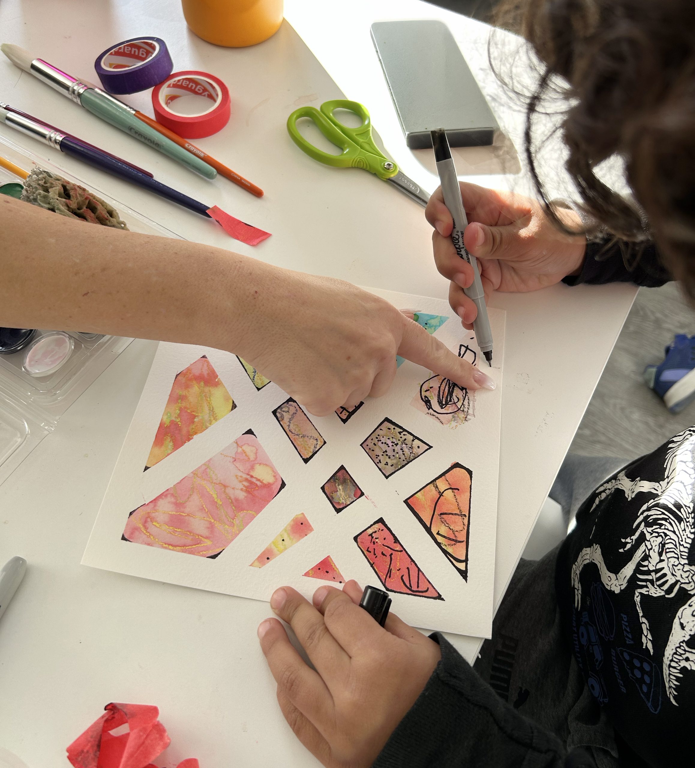 Un enfant dessine au feutre dans des formes géométriques colorées, guidé par la main d’un adulte.